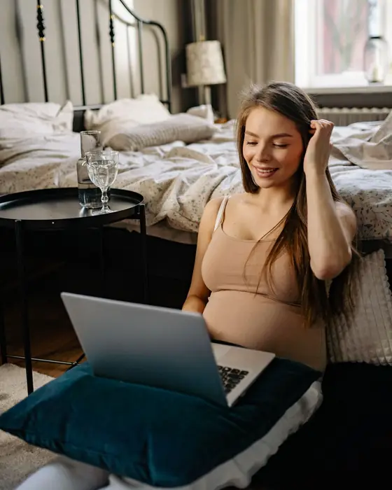 A smiling pregnant woman sitting at home with a laptop